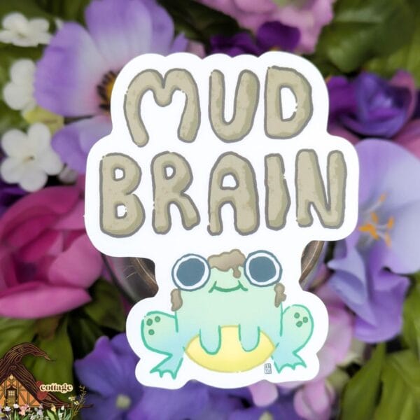 This sticker features a cute little green and yellow frog staring straight ahead with a pile of mud on his head with "mud brain" written in mud above on a white background.
